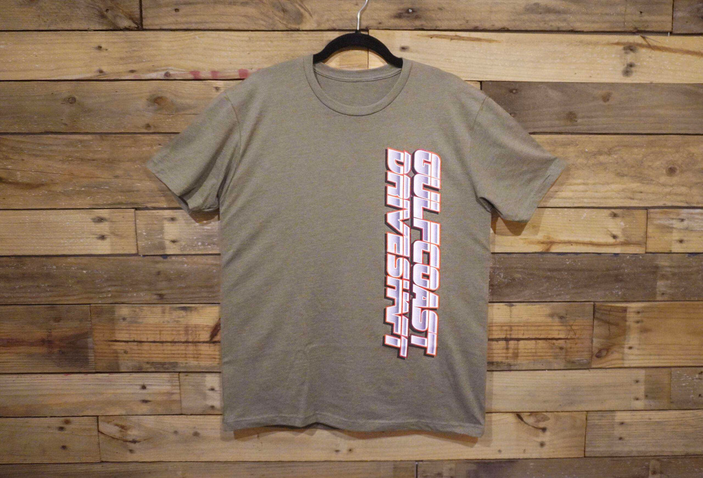 Olive green crewneck t-shirt with "Gulf Coast Driveshaft" logo printed vertically in bold pink and white letters.