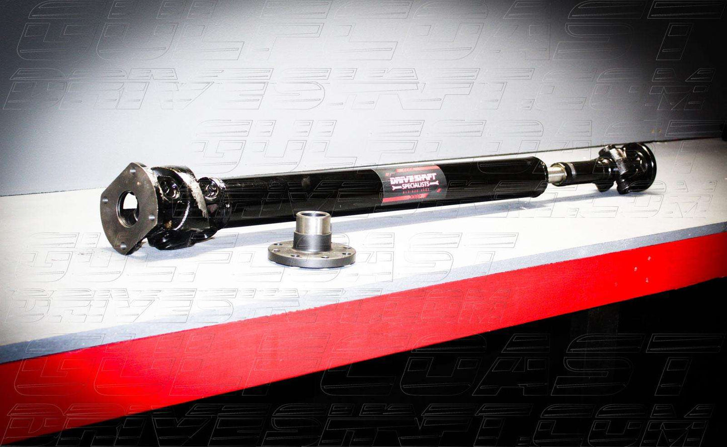 Black 1350 Series rear driveshaft with U-joints and flanges, resting on a gray surface with a red edge, designed for 2018+ Jeep JL 4-door.
