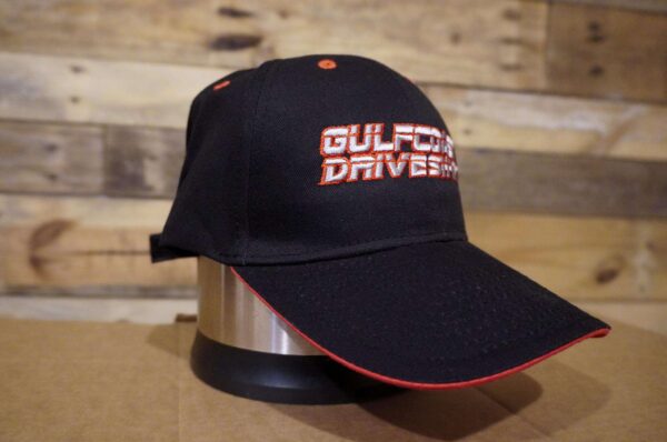 Black Gulf Coast Driveshaft Hat with a pre-curved visor, contrasting red trim, and a Velcro adjusting strap.