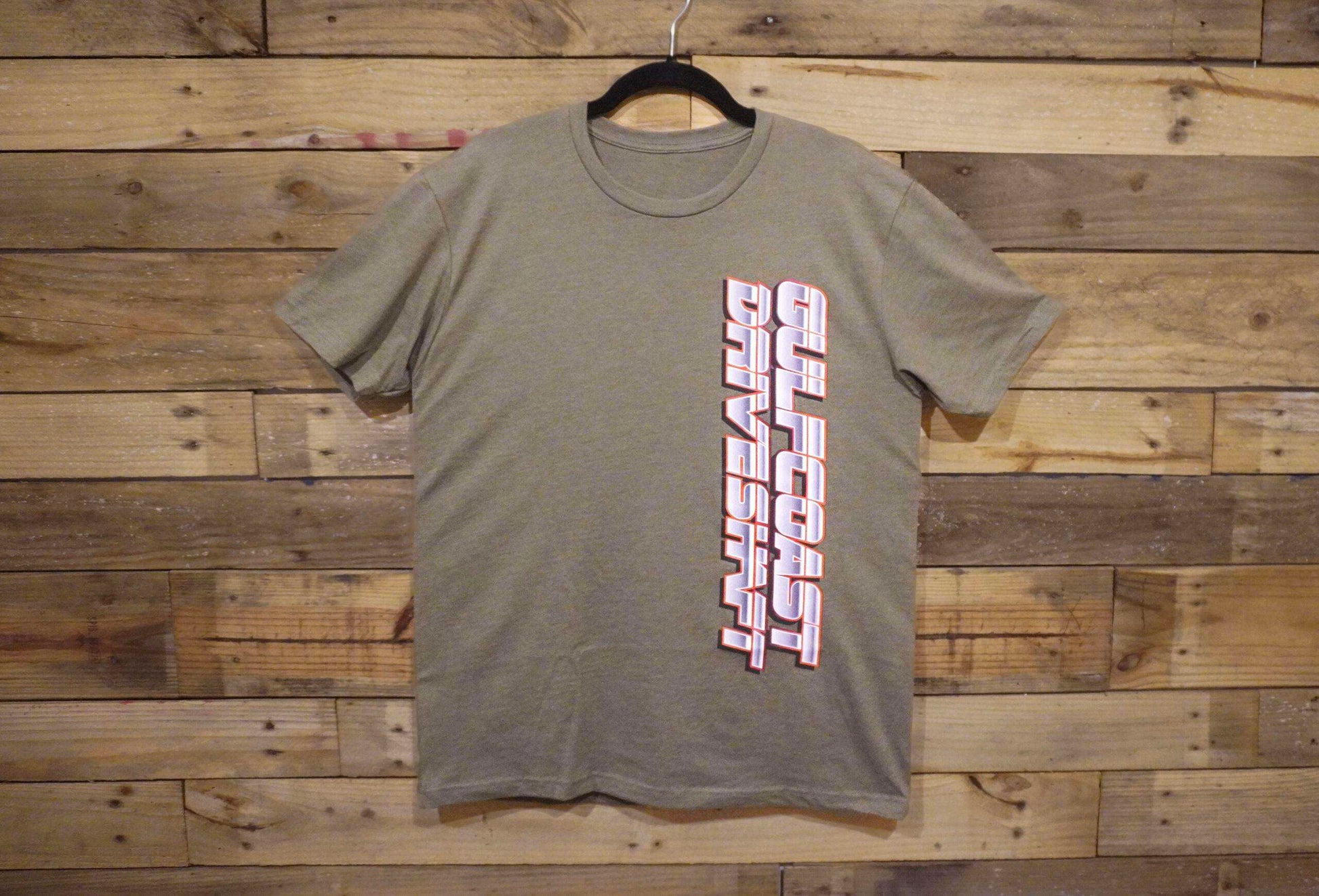 Olive green crewneck t-shirt with "Gulf Coast Driveshaft" logo printed vertically in bold pink and white letters.